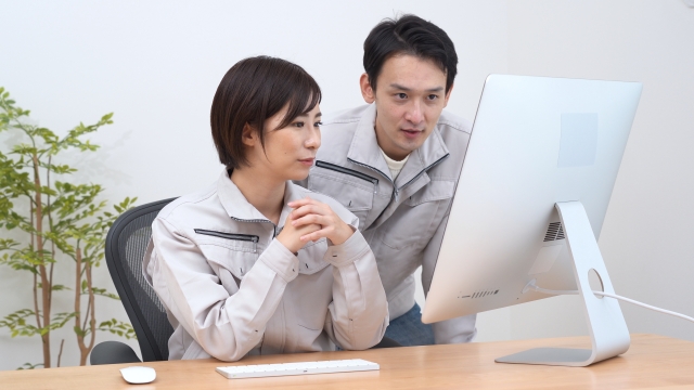 パソコンの画面を一緒に確認する作業着姿の男女